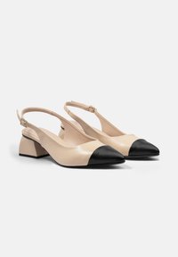 Pantofi slingback din piele bej cu bot cu vârf negru, toc mic și strap ajustabil. Textură netedă cu un design minimalist.