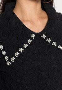 Maglione nero in lana con colletto ampio, decorato con grappoli di ornamenti simili a perle lungo il décolleté in motivi floreali.