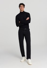 Czarny sweter z golfem i długimi rękawami, w połączeniu z czarnymi spodniami i białymi trampkami. Gładka faktura, dopasowany krój i prosty design.