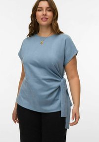 Haut à manches courtes bleu clair en tissu doux, avec un détail de nœud sur le côté et une coupe décontractée, associé à un pantalon noir.