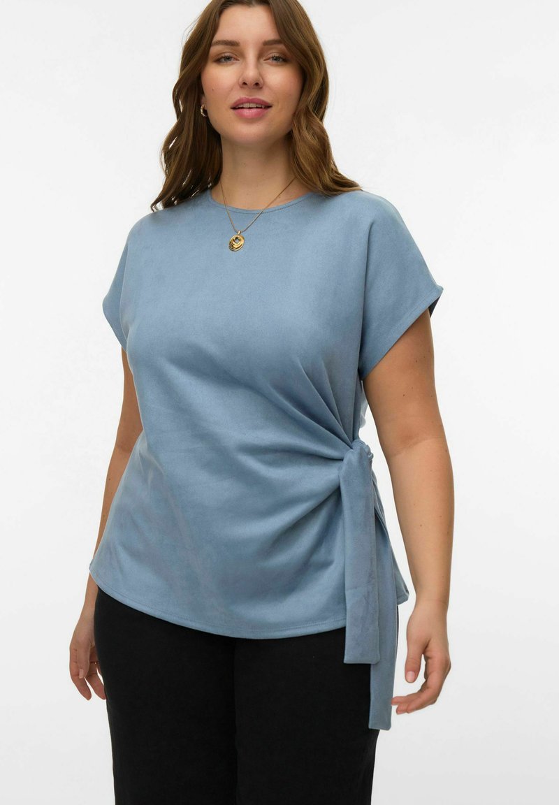 Haut à manches courtes bleu clair en tissu doux, avec un détail de nœud sur le côté et une coupe décontractée, associé à un pantalon noir.