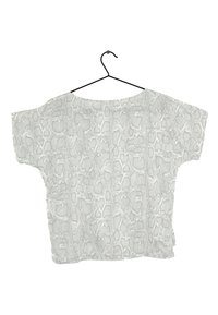 Blusa grigia a maniche corte con motivo a stampa serpente appesa a un gancio in metallo nero su uno sfondo bianco.