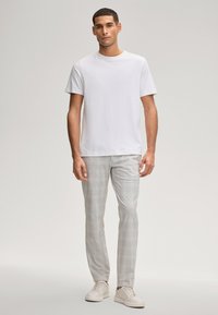 Wit katoenen T-shirt gecombineerd met lichtgrijze geruite broek en witte sneakers. Eenvoudig ontwerp en losse pasvorm met korte mouwen.