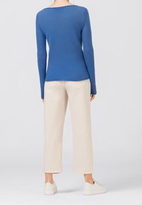 Blauer, langärmliger Strickpullover mit rundem Ausschnitt, kombiniert mit hellbeigen, weiten Hosen und weißen Sneakern. Minimalistisches Design.