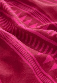 Textilstoff in tiefem Pink mit geometrischen Mustern, darunter Dreiecke und Streifen, der eine weiche Textur und einen lebhaften Farbkontrast zeigt.