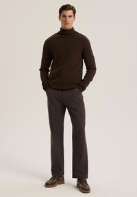 Brązowy sweter z golfem i długimi rękawami, zestawiony z ciemnoszarymi spodniami i brązowymi butami brogue, tworzący spójny, dopasowany wygląd.