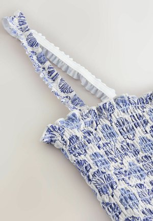 Material alb și albastru cu imprimeu smocked și modele cu scoici, cu bretele elastice ruffle pe un articol vestimentar fără mâneci.