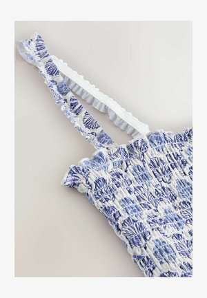 Material alb și albastru cu imprimeu smocked și modele cu scoici, cu bretele elastice ruffle pe un articol vestimentar fără mâneci.