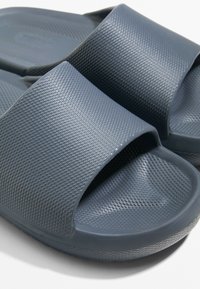 Grijze rubberen slidesandalen met een gestructureerde bovenband en een gladde voetbed, ontworpen voor comfort en eenvoudig draaggemak.