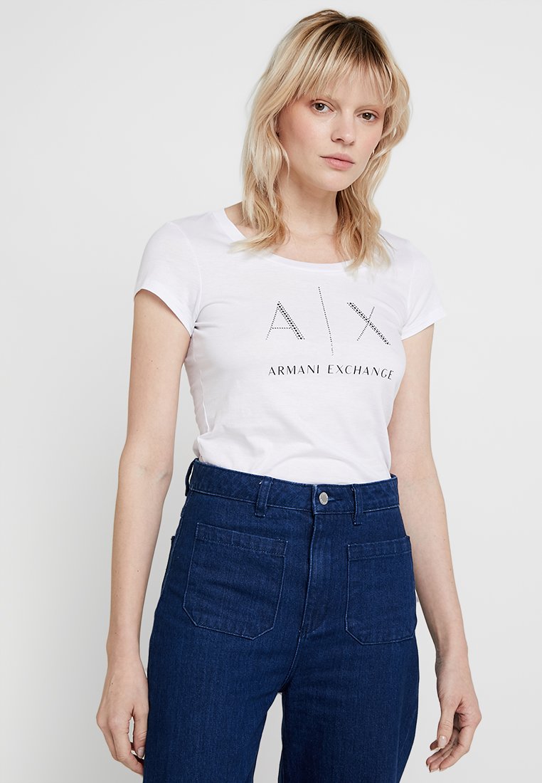 Vit bomull t-shirt med "A|X ARMANI EXCHANGE" i nitar, tillsammans med höga mörk denimjeans med framfickor.