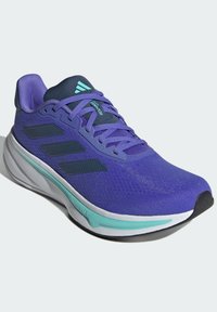 Zapatilla deportiva morada con parte superior de malla, tres franjas negras, acentos en azul agua y una suela blanca. Presenta un diseño acolchado para mayor comodidad.