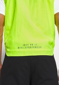 Nike sportstop i lys neongrön med strukturerad yta. Har "JUST DO IT" och "NIKE SPORTSWEAR" tryckt längst ner.