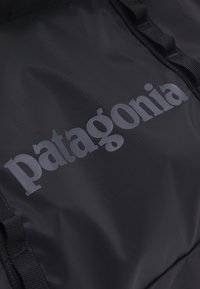 Črna tkaninska nahrbtnik z izrazitim sivo "patagonia" logotipom, teksturiran najlonov material in trdni trakovi.