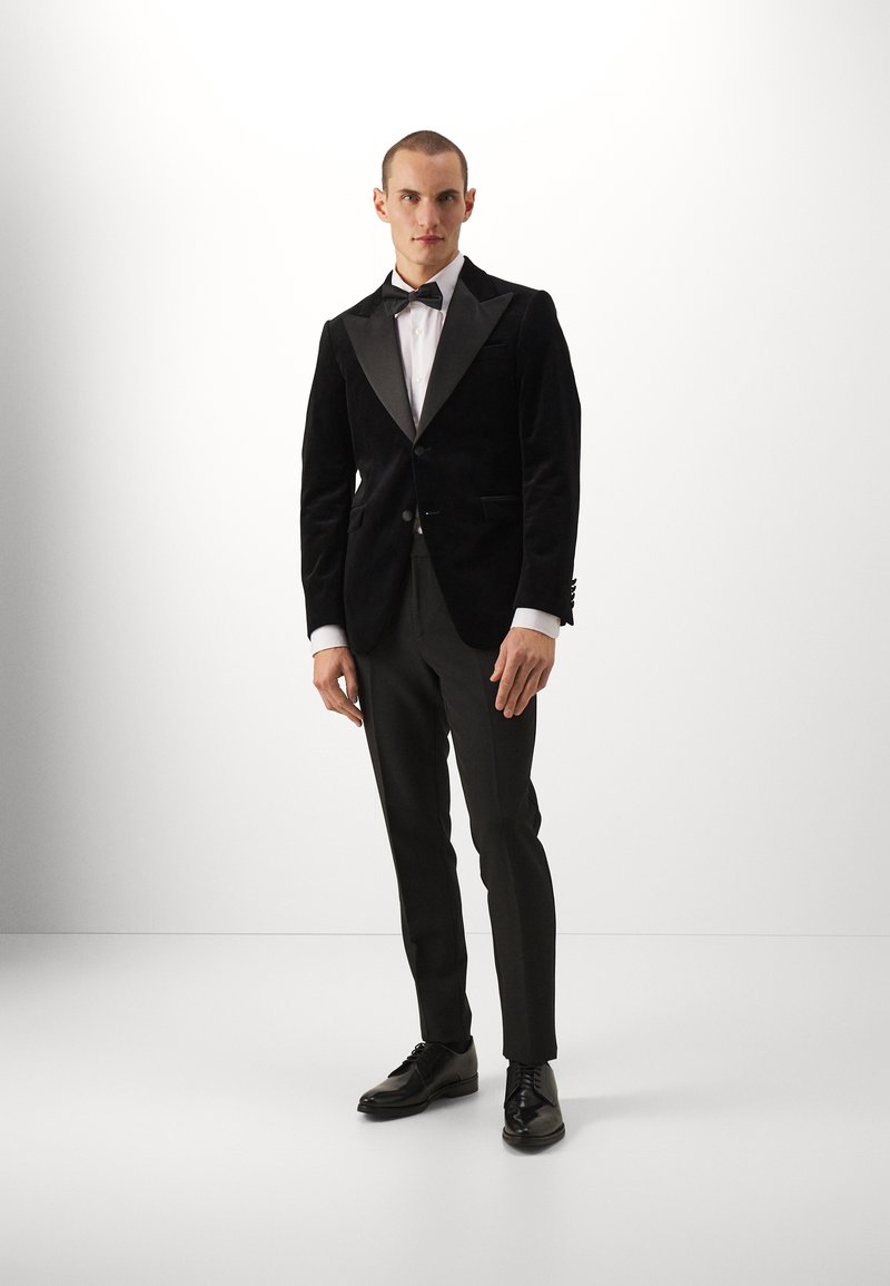 Czarna aksamitna marynarka smokingowa z satynowymi klapami, biała koszula, czarna muszka oraz skrojone czarne spodnie. Błyszczące czarne buty muzyczne.