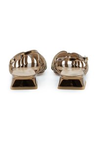 Zapatos abiertos en bronce con tacón cuadrado plano, que presentan un diseño de tira trenzada y adornos decorativos a lo largo de la parte superior.