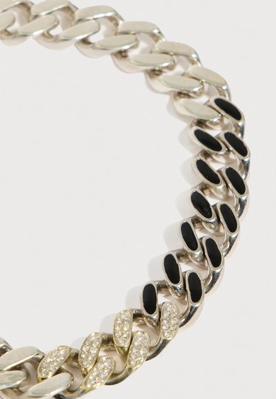 Collier en chaîne argentée avec des maillons alternant entre émail noir et petits cristaux incrustés, sur fond blanc.