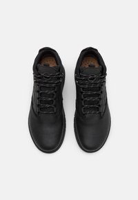 Scarpe nere in pelle con superficie testurizzata, dotate di lacci neri, colletto imbottito e soletta di un marrone chiaro con motivi a punti.
