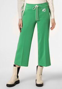 Pantaloni larghi verdi realizzati in tessuto morbido, con una vita con cordoncino e un logo bianco vicino all'anca. Abbinati a stivali alla caviglia color crema.