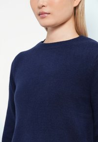 Pulover tricotat de culoare bleu marin, cu guler rotund și mâneci lungi, având o textură moale și un finisaj de țesătură neted.