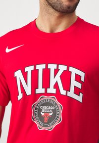Punane puuvillane T-särk, millel on suurtes valgetes tähtedes sõna "NIKE" ja selle all keskjoonel Chicago Bullsi ringikujuline logo. Ühel õlal on valge Nike'i sving.
