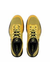 Zapatillas deportivas amarillas con parte superior de malla, acentos negros y suelas blancas. El diseño incluye cordones y un logotipo de la marca visible en el lateral.