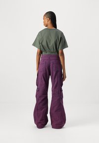 Afgeknot olijfgroen t-shirt gecombineerd met losse paarse cargobroek met zijzakken en een gestructureerde afwerking.