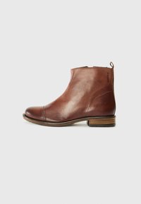 Bottines en cuir marron avec un design épuré, bout arrondi, petit talon empilé et détails de couture sur les côtés. Dotées d'une languette à l'arrière pour plus de facilité.