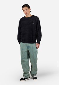 Sort, fluffy sweater med rund halsudskæring og hvidt logo. Båret med løse, lyseblå jeans med sidelægning og hvide detaljer. Sorte sneakers.