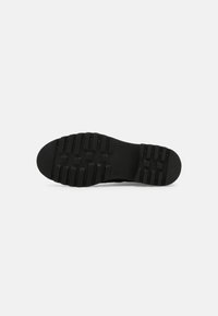 Suela de zapato de goma negra con un patrón de relieve texturizado, que presenta surcos horizontales y verticales para tracción. Acabado suave en general.