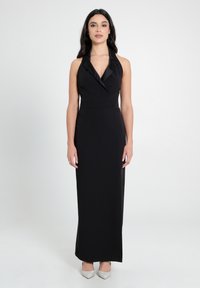 Schwarzes Halterneck-Abendkleid mit einer figurschmeichelnden Silhouette, das einen Satin-Kragen und einen bodenlangen Schnitt aufweist. Akzentuiert mit silbernen High-Heels.