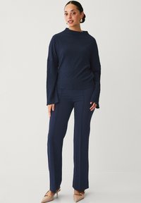 Marineblå struktureret sweater med lange ærmer, parret med skræddersyede marineblå bukser med lige ben. Model iført nude flade sko med accenter.