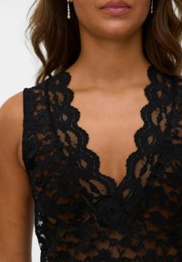 Sort blonde top med en dyb V-udskæring, blomsterdesign og bølgede kanter. Den glatte tekstur med gennemsigtige sektioner fremhæver designet.