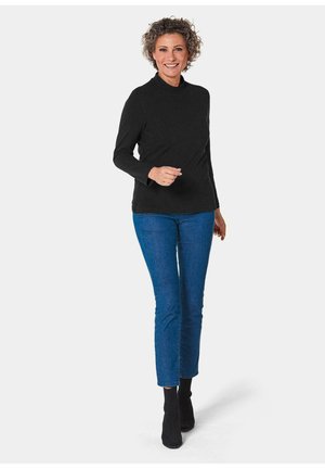 Schwarzes langärmliges Rollkragenoberteil, kombiniert mit blauen Skinny-Jeans und schwarzen Stiefeletten. Glatter Stoff mit einer figurbetonten Passform, ohne Muster.