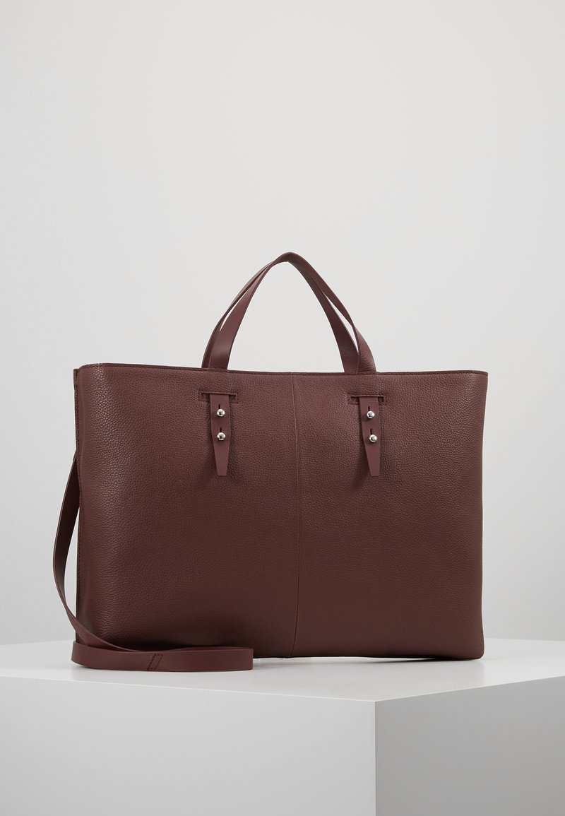 Sac cabas en cuir marron texturé avec deux poignées supérieures, une longue bandoulière et des détails de clous argentés sur les sangles avant.