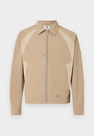 Giacca beige con zip, pannelli beige chiaro sulle spalle, colletto appuntito, tasche anteriori, bottoni automatici e piccola toppa logo vicino all'orlo.