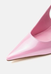 Γυαλιστερό ροζ γυναικείο παπούτσι με ψηλό τακούνι και μυτερή μύτη, με λεία επιφάνεια σε λευκό φόντο, που αναδεικνύει το μπροστινό και το πλευρικό περίγραμμα του παπουτσιού.