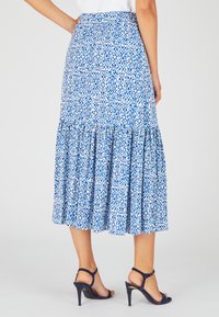 Gonna maxi a fantasia blu e bianca con design a strati, cintura elastica e silhouette fluida. Abbinata a sandali con tacco alti blu navy.