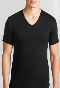 T-shirt nera a maniche corte con scollatura a V. Realizzata in un tessuto morbido, design aderente e dettagli di cucitura minimalisti lungo il colletto.