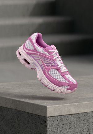 Pantof de alergare Nike roz și alb din plasă, cu talpă mijlocie cu amortizare cu aer vizibilă, plutind deasupra unei margini de beton gri, cu un fundal de trepte neclar.