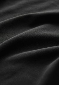 Gros plan d’un tissu noir lisse avec des plis doux et une texture mate, mettant en avant le tissage fin et les nuances subtiles du matériau.
