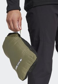 Olive green, rectangular, padded pillow with a mesh side and a carrying strap, held in a hand; attached label displays product details.
