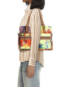 Bunte Tragetasche mit geometrischem Muster, ausgestattet mit braunen Lederträgern und einer vorderen Reißverschlusstasche. Das Material wirkt synthetisch und glänzend.