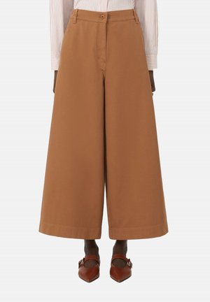 Pantaloni marroni a gamba larga e tagliati, indossati con scarpe Mary Jane marroni con punta appuntita e camicia a righe a manica lunga.