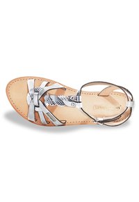 Sandal in argento con cinturini intrecciati e texture rettile. Presenta una suola piatta e una cinghia alla caviglia, posizionata su una soletta beige.