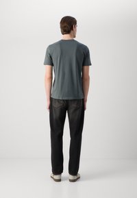 Mørkegrå t-skjorte med kort erme og rund hals, kombinert med svarte jeans. Jeansene har baklommer og en avslappet passform.