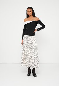 Õlgadeta must topp, millel on valge aktsent; kombineeritud valge seelikuga, millel on musta kirjatüübi mustrid, ja mustade kontsakingadega.