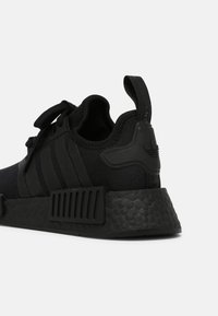 Czarne sneakersy z siateczkowym wierzchem, trzema czarnymi paskami, teksturowaną czarną podeszwą i pętelką. Lekka konstrukcja, idealna do codziennego użytku.