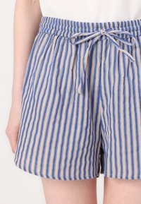 Randiga shorts med dragsko i midjan, gjorda av ett lätt tyg. Blåa och beige ränder som löper vertikalt med en avslappnad passform.