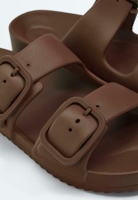 Bruine sandalen met open neus, voorzien van twee verstelbare brede banden met grote vierkante gespen en gevormde voetbedden.