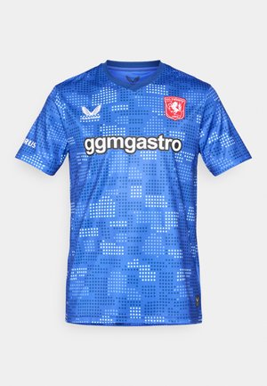 Maillot de football bleu avec un col en V, présentant un motif pixelisé, un logo sur la poitrine gauche et le texte "ggmgastro" sur le devant.